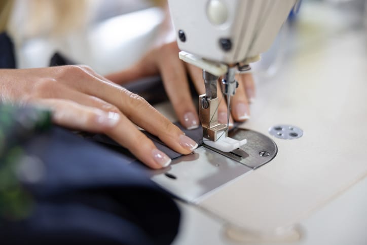 Close-up on a seamstress sewing clothes at an atelier on a machine